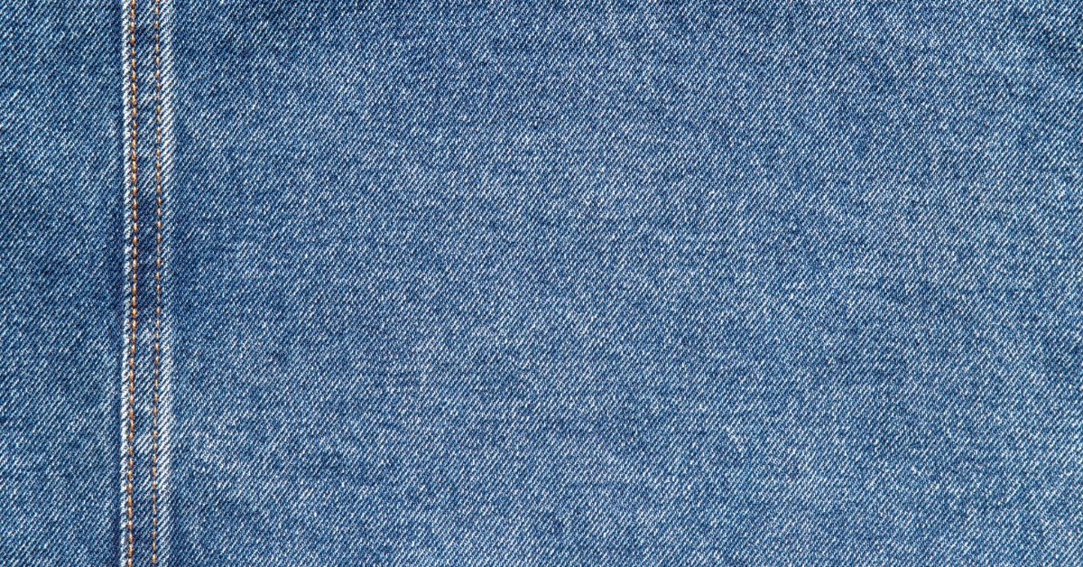 Blue denim fabric with a vertical stitched seam along the left side and visible diagonal woven texture.