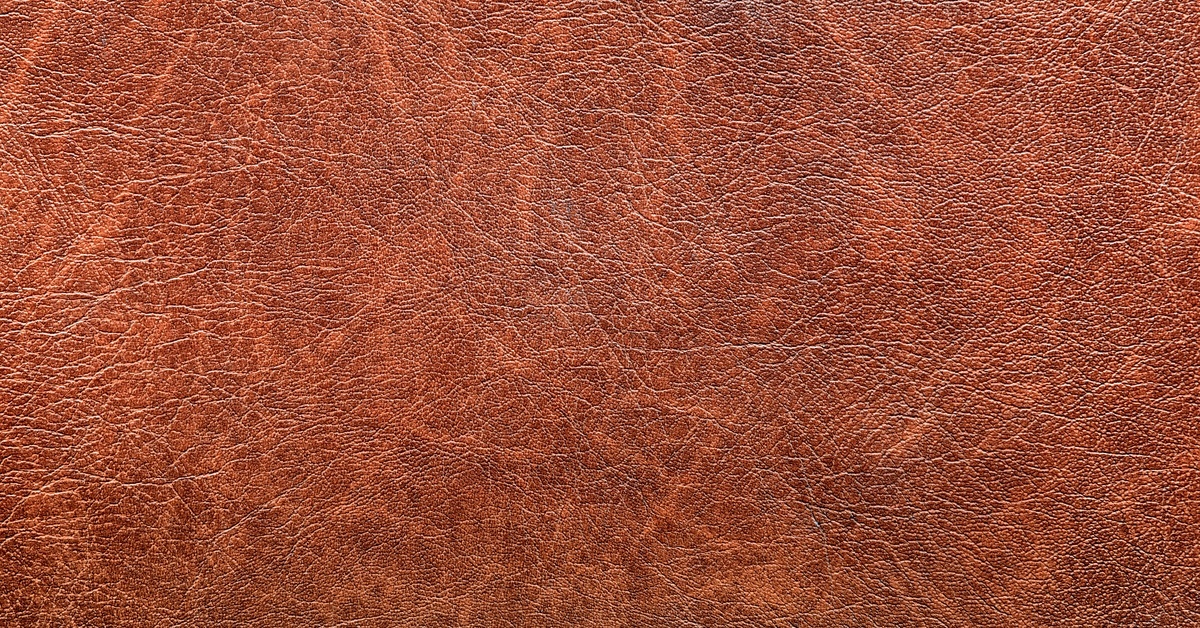 A reddish brown leather surface with fine creases, scratches, and uneven texture covering the entire area.