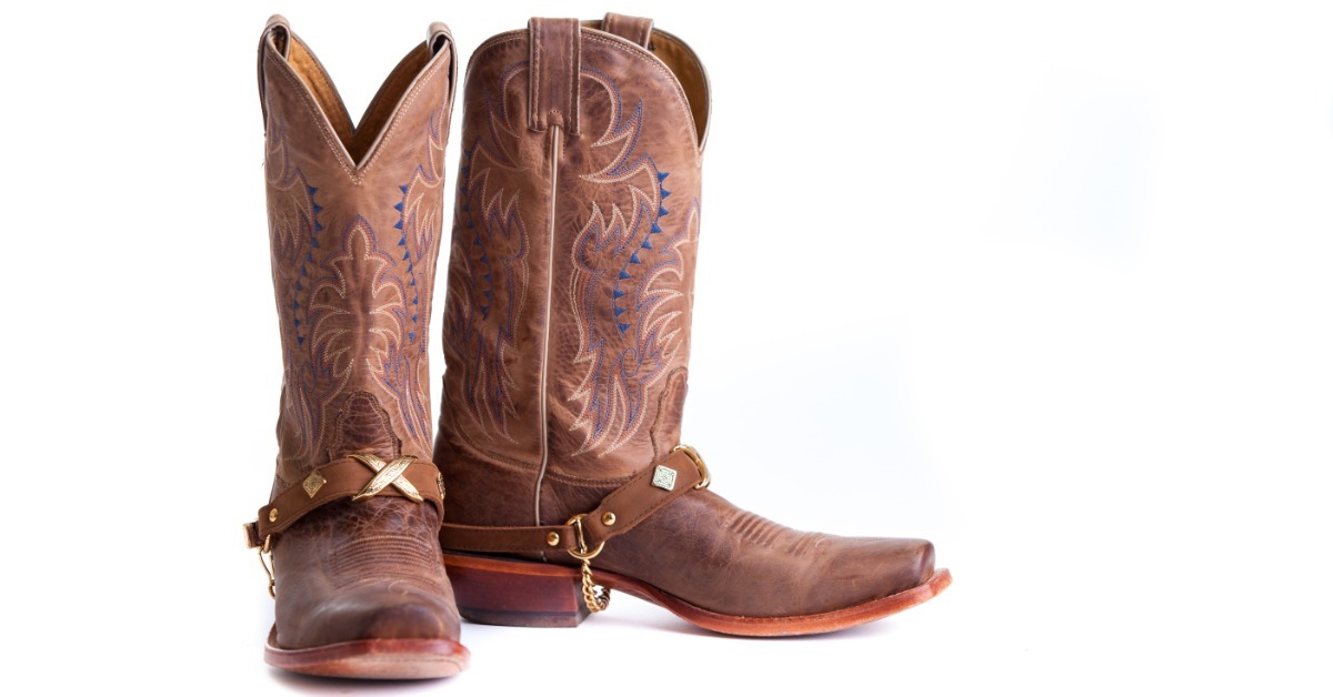 A pair of brown cowboy boots with decorative blue stitching and metal straps standing against a white background. A pair of brown cowboy boots with decorative blue stitching and metal straps standing against a white background.