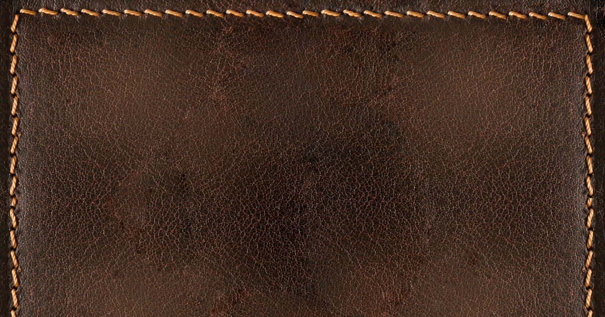 A dark brown leather surface with visible textured grain and tan stitching running around the outer edges. A dark brown leather surface with visible textured grain and tan stitching running around the outer edges.