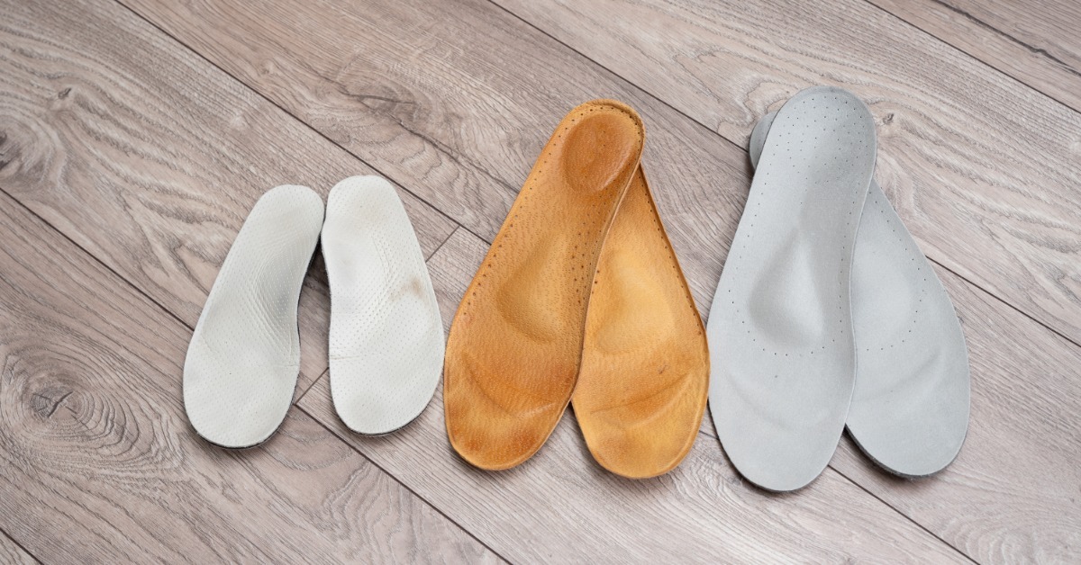 Three pairs of white, tan, and gray shoe insoles lying side by side on a light wood floor in different sizes.