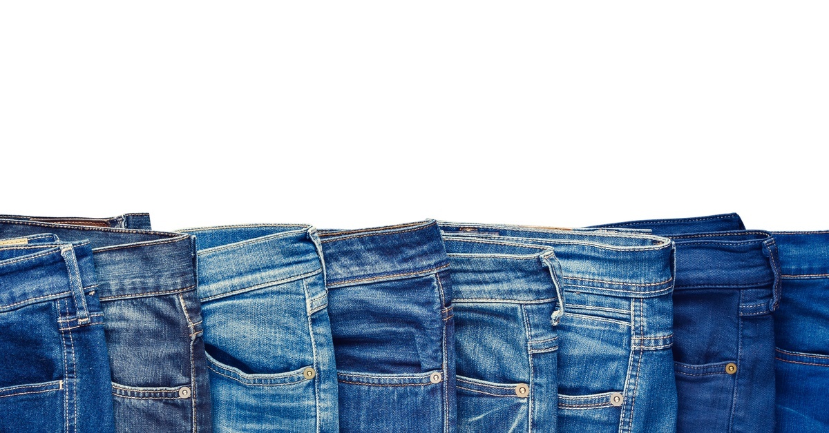 A row of blue jeans in different shades and styles. They are laid out on top of each other on a white background.