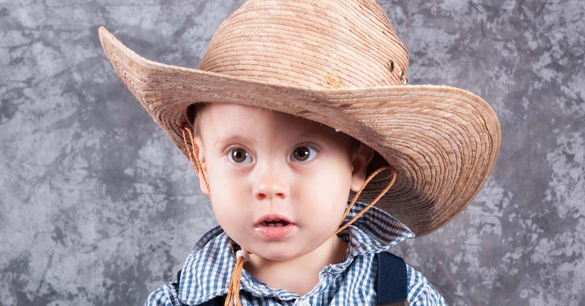 A young toddler wearing a checkered button up shirt and a straw cowboy hat that is too big for him.