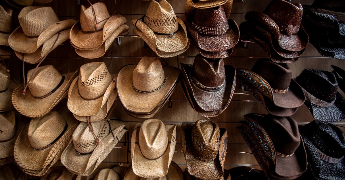 Rows of different cowboy hats on display. They come in tan, brown, and black and feature a variety of brim styles.