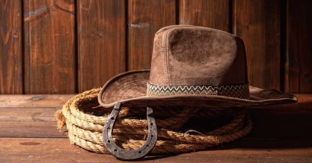 A brown leather cowboy hat resting on top of a coil of rope. A horseshoe leans against the rope.