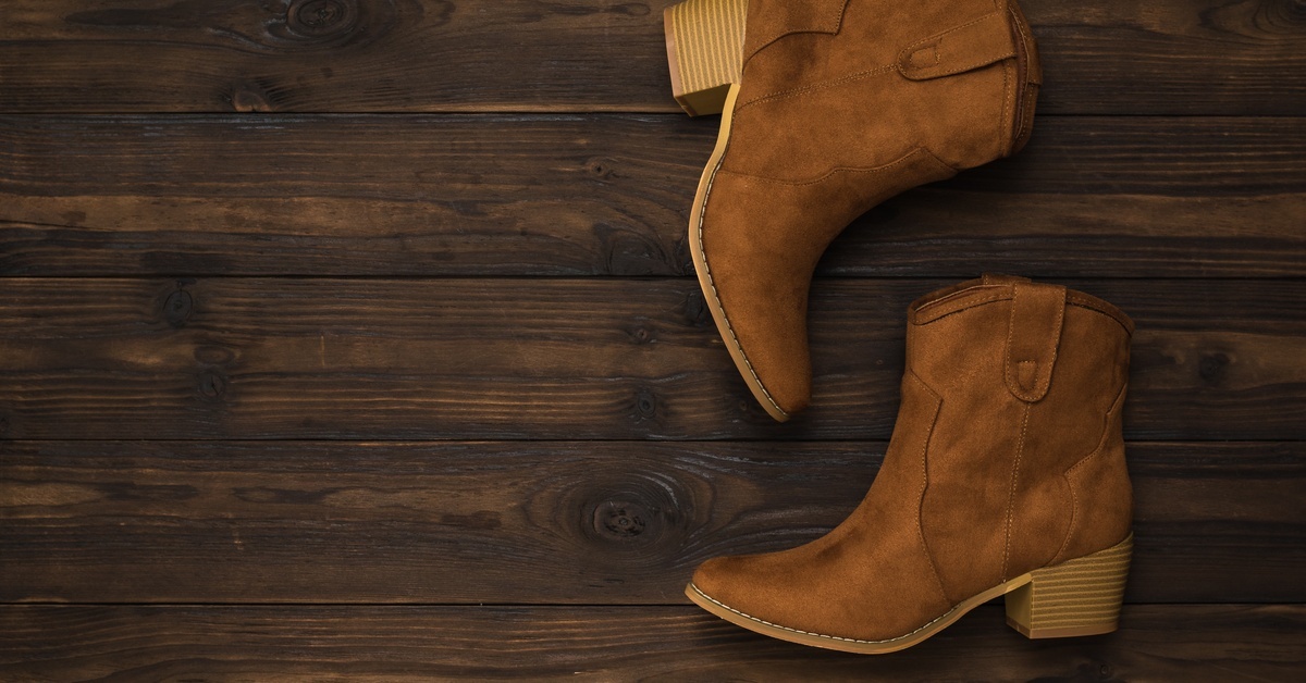 A pair of women's tan suede heeled boots lying on their sides on top of a dark brown wooden surface.
