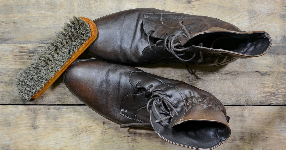 A pair of dark brown leather boots with a soft bristle brush propped up against the toes of the boots.