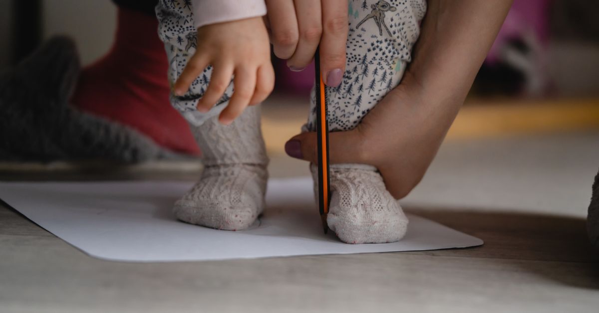 An adult holding a baby's foot down on a piece of paper. They are using a pencil to outline the baby's foot.
