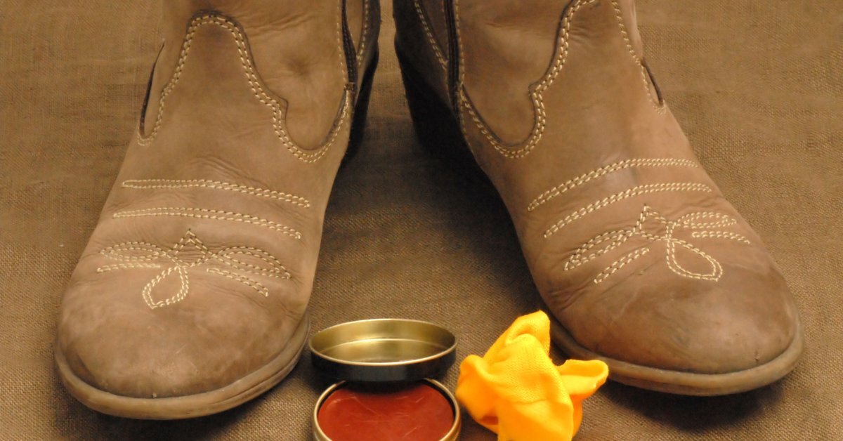 A pair of light brown cowboy boots with heels. A container of polish and a cloth sits between them.