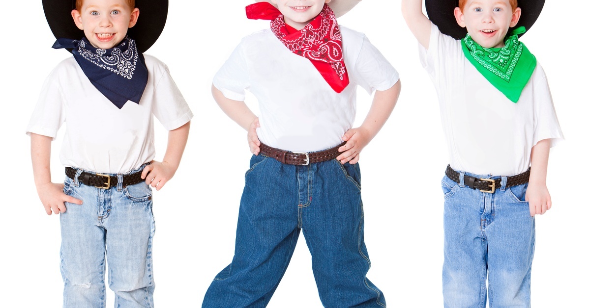 Three little boys wearing jeans, belts, bandanas, and cowboy hats. They are posing and smiling.