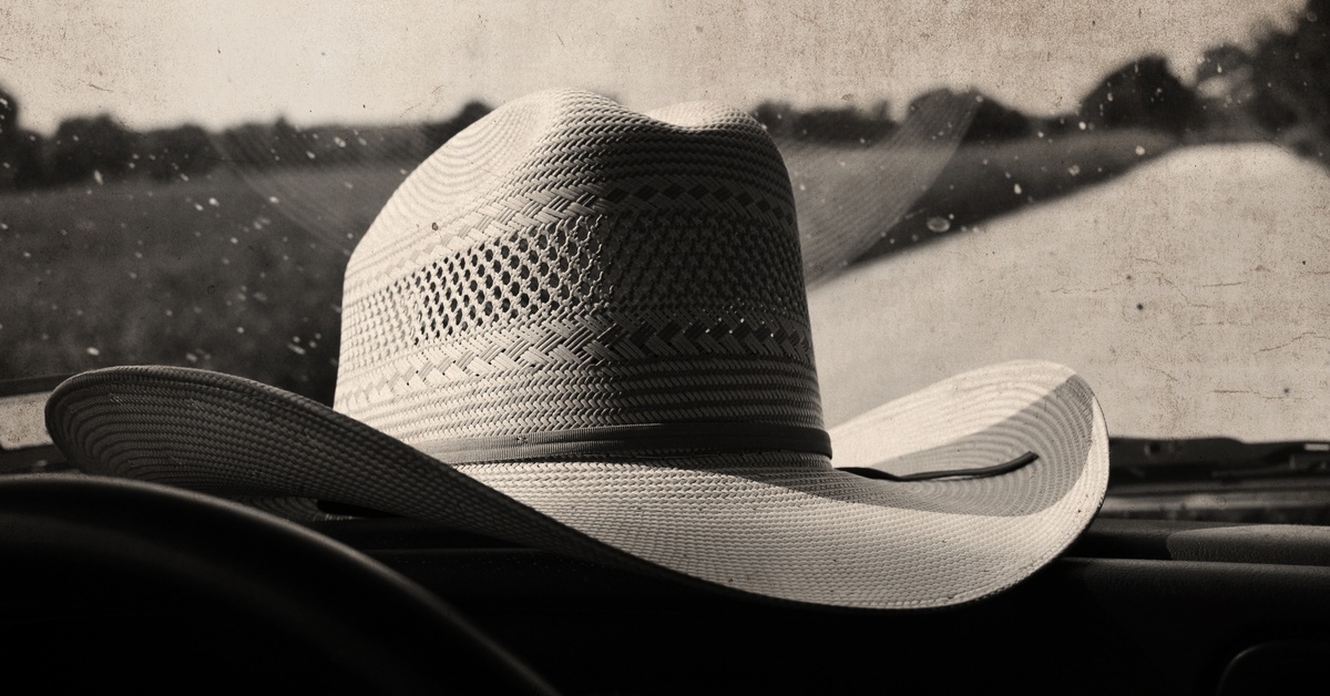 A straw cowboy hat with a tall crown and a dark hat band. It is resting on the dashboard of a car.