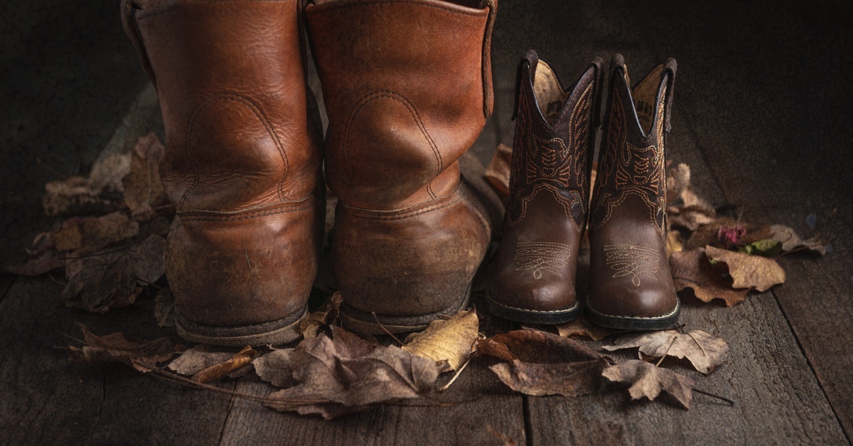 Two pairs of cowboy boots placed next to each other. One pair is adult-sized, while the other is child-sized.