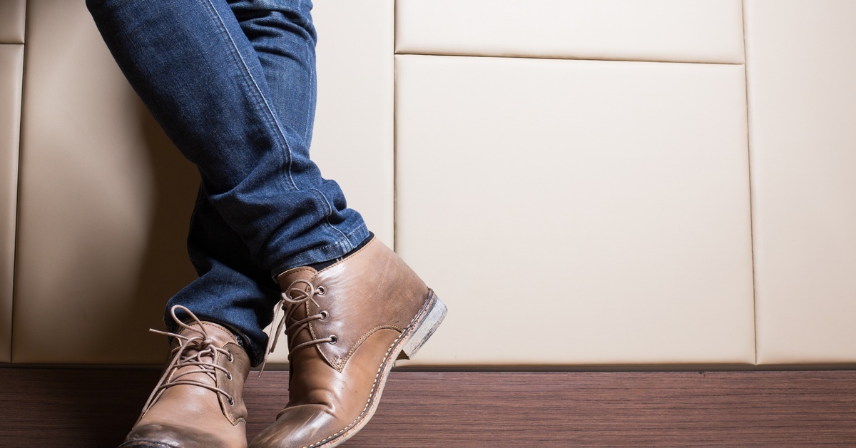 A person wearing blue jeans and short leather cowboy boots leaning against a plush, white leather wall.