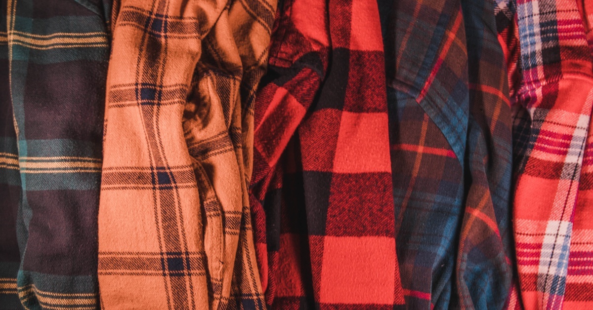 Multiple flannel shirts placed in a row with varying colors, such as dark green, orange, red, and scarlet.