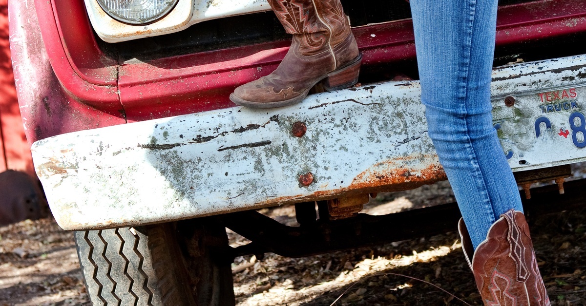 Boot Styles Every Western-Loving Girl Needs A woman in jeans leans one leg on the front bumper of a red vehicle, showing off one of her brown boots.