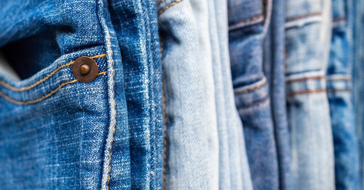 A hanging row of several pairs of stylish jeans, all in the same size, in various colors and washes.
