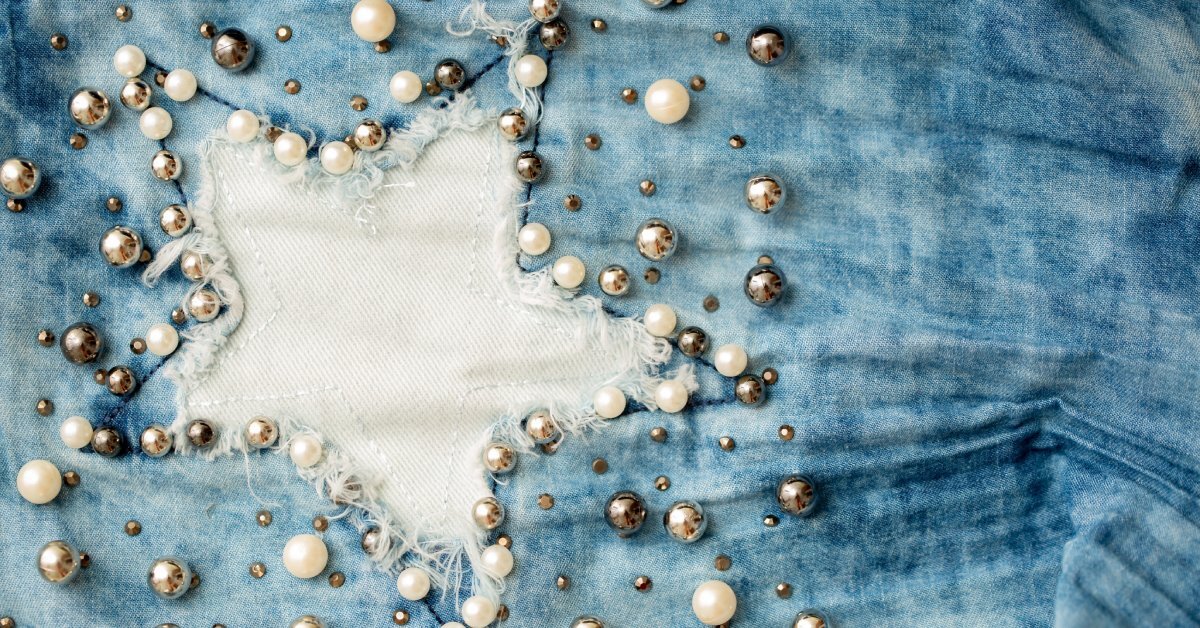 A close-up of a star-shaped cutout on denim fabric, surrounded by small, embroidered pearl-like beads.
