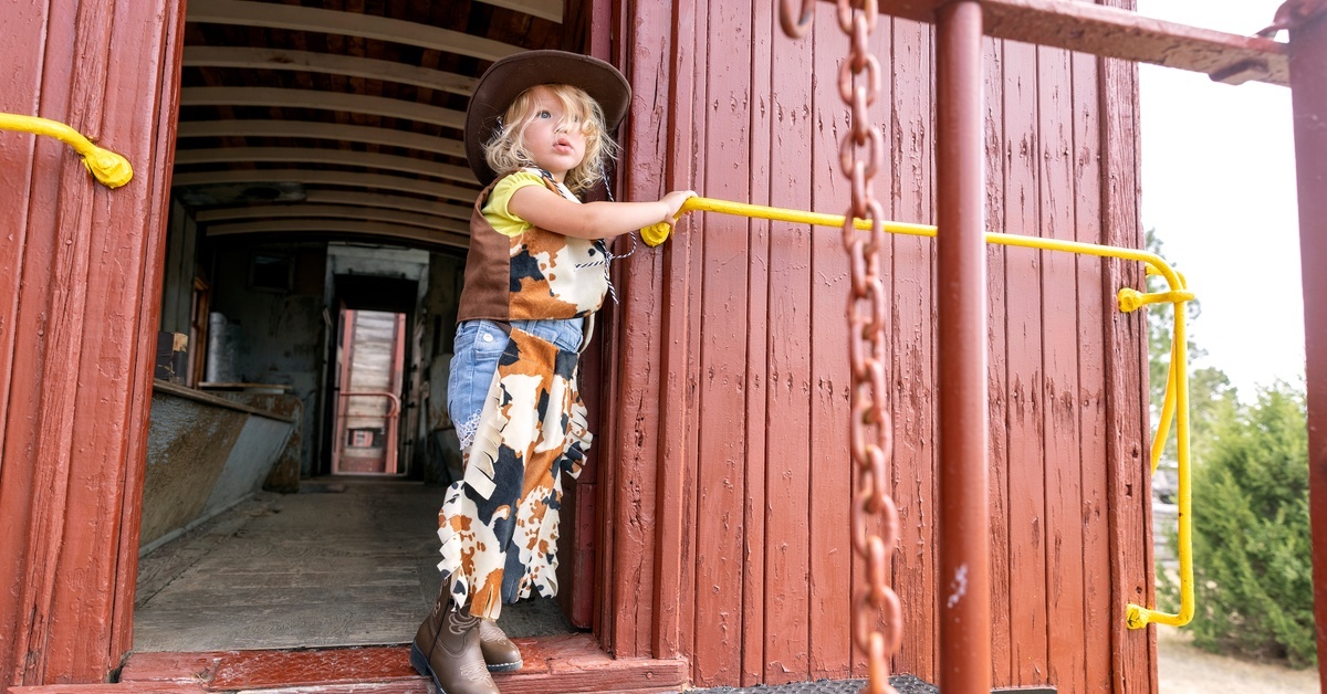 A child dressed in Western attire, including cowboy boots, striking a pose in the doorway of a vintage train car.