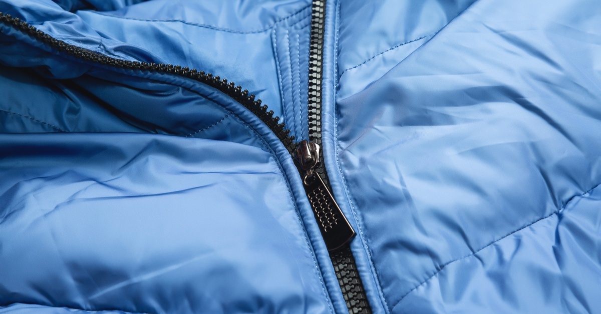 A close-up of a blue winter bubble jacket with a slightly wrinkled texture and a partially unzipped black zipper.