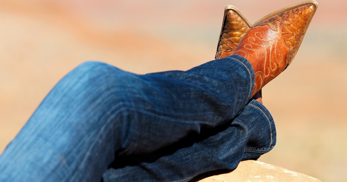 A pair of legs wearing straight-cut dark wash jeans, with detailed cowboy boots peeking out from underneath.