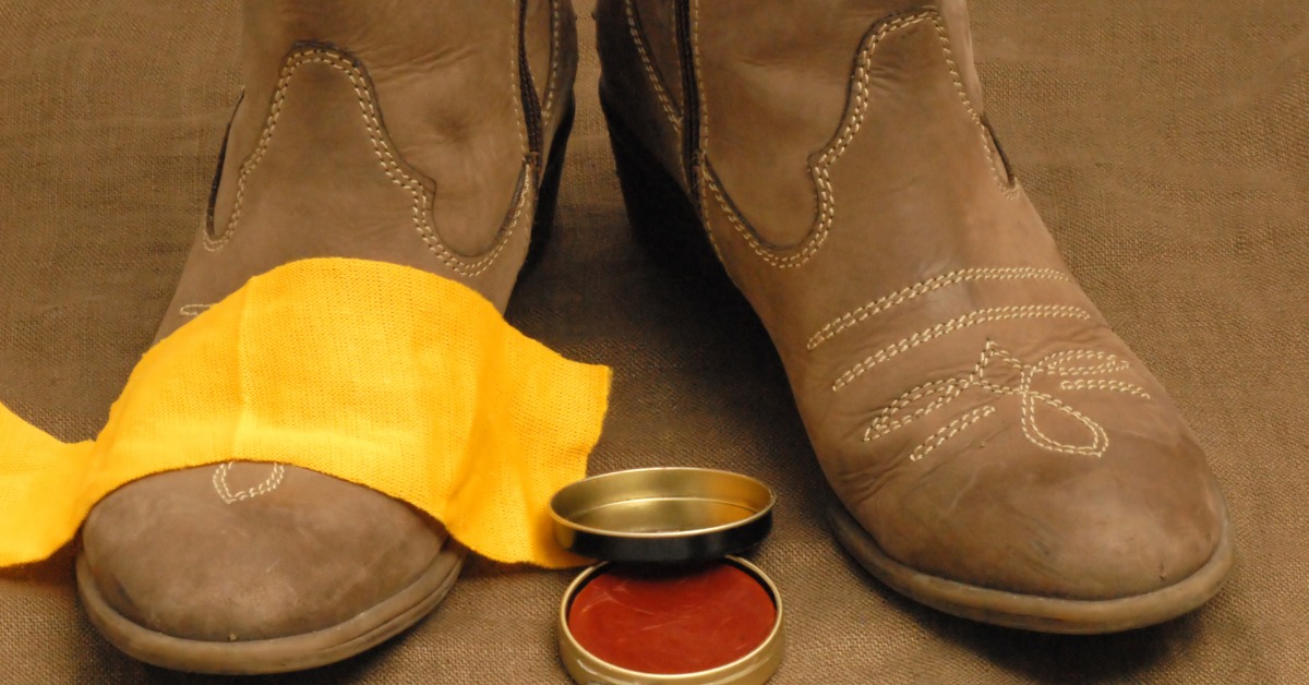 Cowboy boots. There's a yellow cloth over the boot on the left, and a container of leather conditioner in front of the pair.