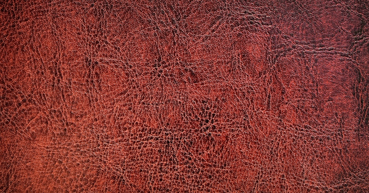 An extreme close-up on a red leather surface. The leather is aged, with cracks and a deep, rich patina.