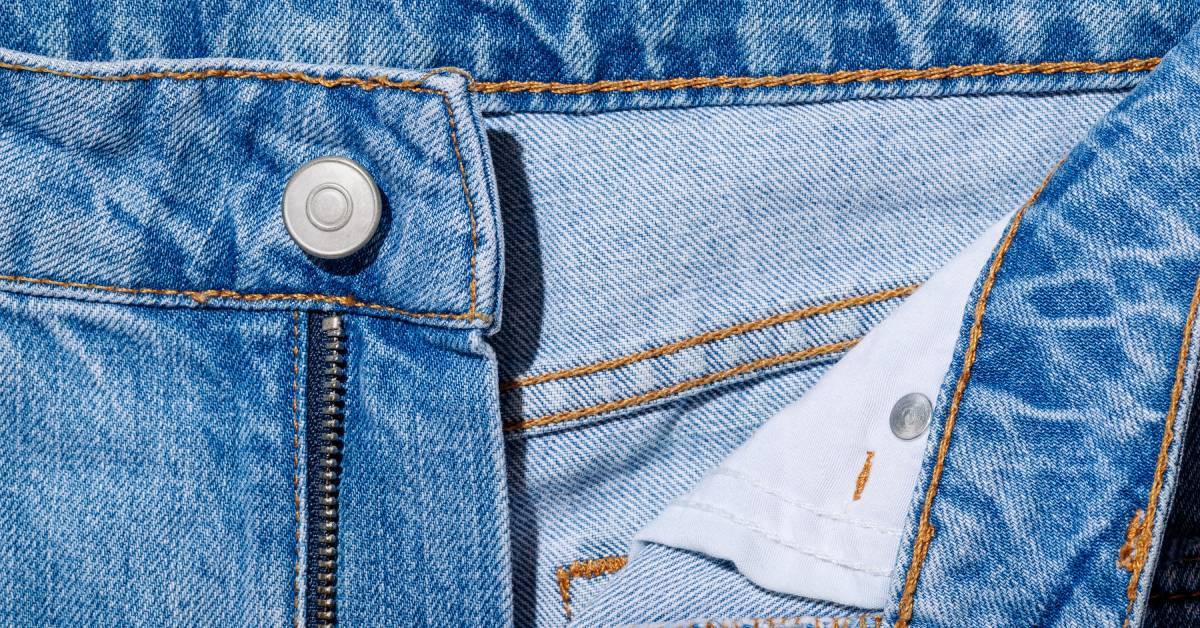 A close view of blue denim jeans with the zipper partially open showing the metal zipper teeth and waistband.
