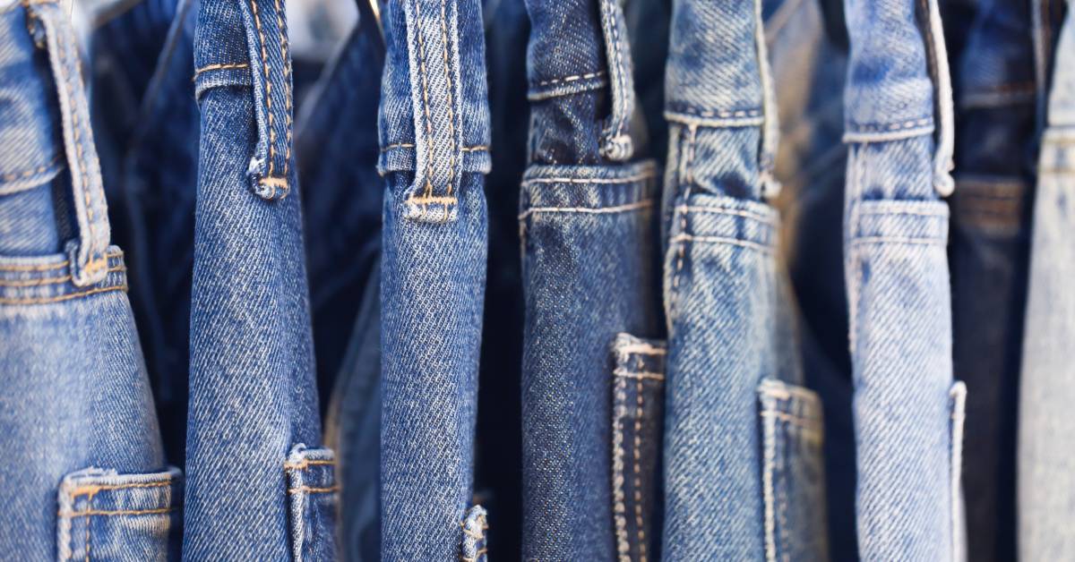 A row of blue denim jeans hanging on a rack with different shades and styles displayed side by side.