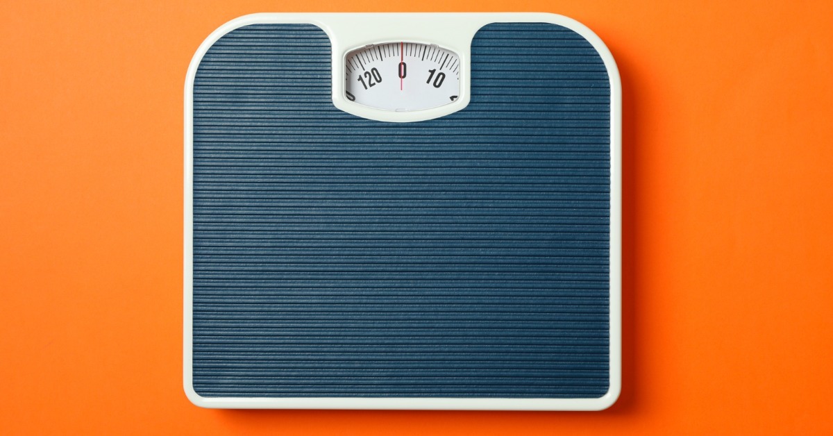 A blue mechanical scale viewed from above on a solid orange surface with empty space around the object.