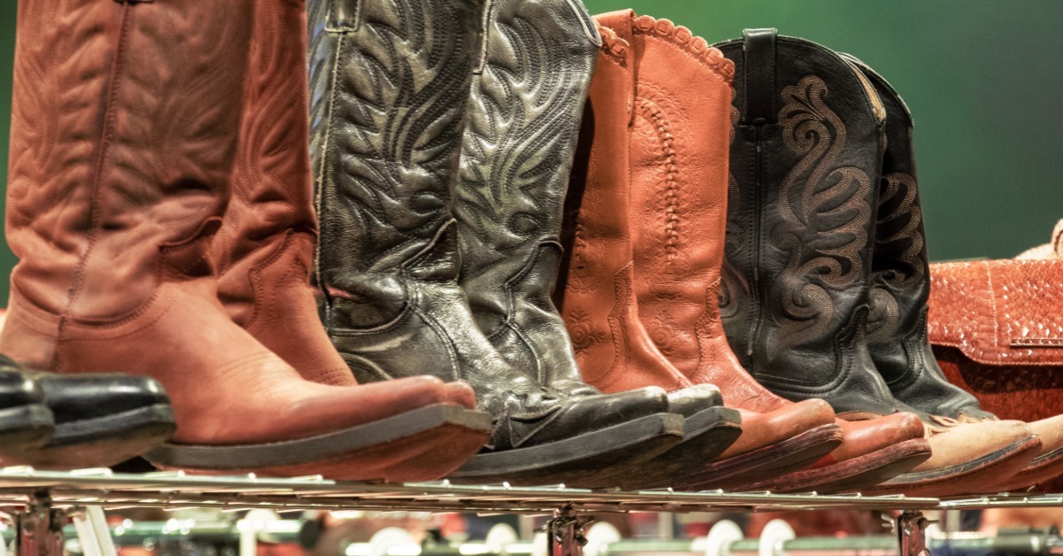 Several pairs of brown and dark leather western boots standing upright on a metal rack inside a store.