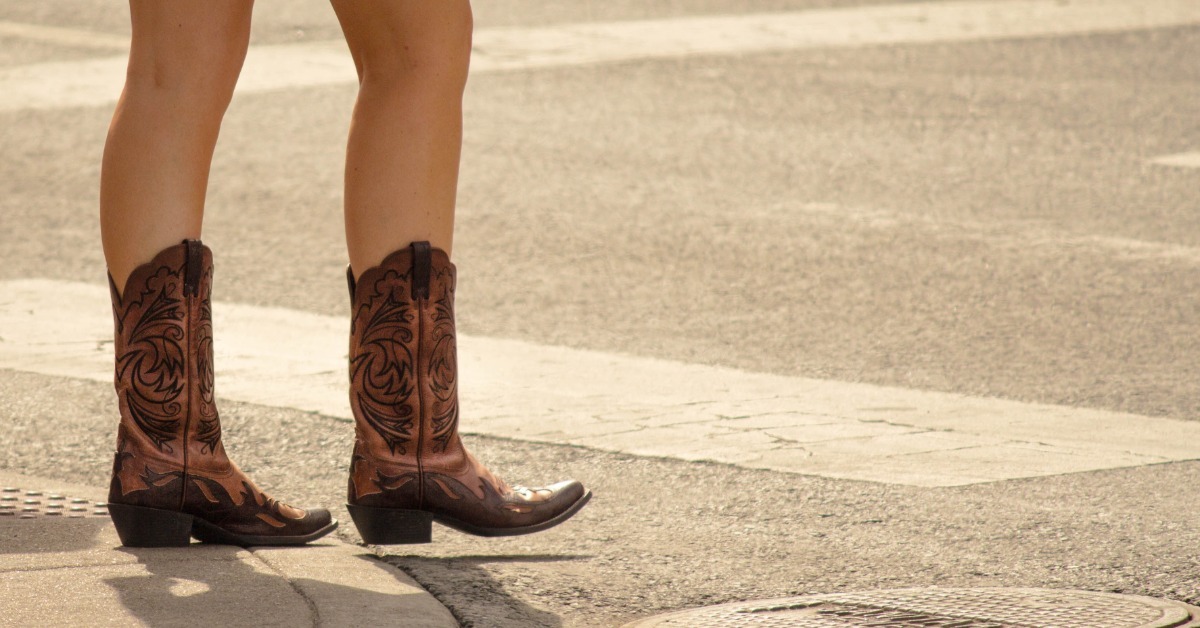 A woman wearing decorative western boots walking down a crosswalk, with a close-up view of her legs.