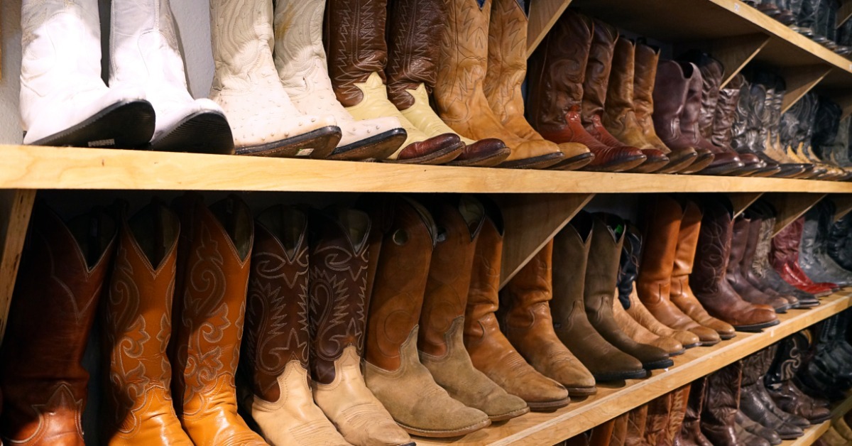 Several pairs of cowboy boots with assorted designs lined up on a light-colored wooden shoe rack against a wall.