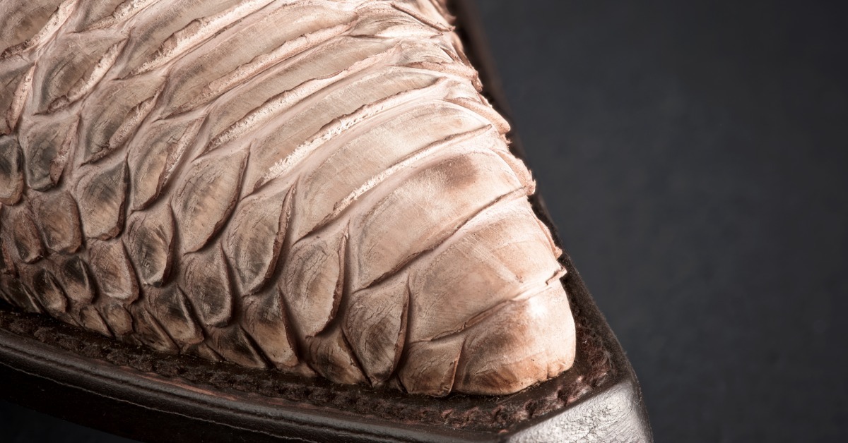 A close detail of a pale textured cowboy boot toe with layered scales, dark edging, and a black background.